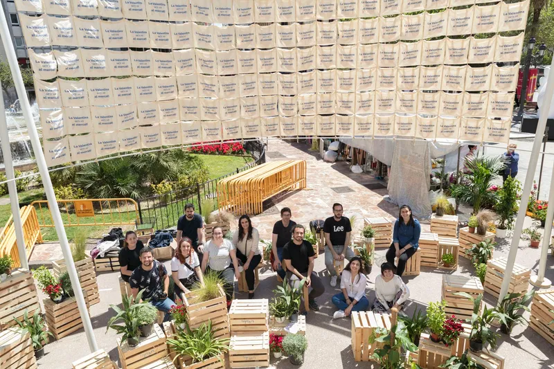 Overhead view of an open courtyard with timber benches and planters under a suspended textile canopy