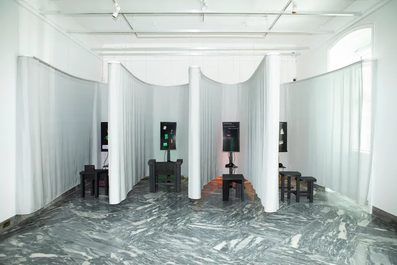 Exhibition space with curved white curtain partitions and swirling grey marble floor under track lighting