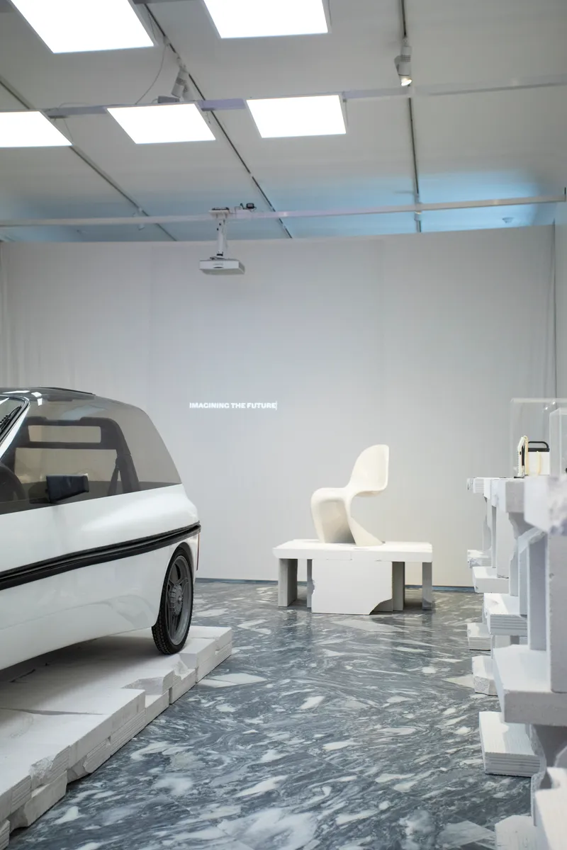 White exhibition room with gridded ceiling and marbled grey floor showing sculptural furniture arrangements