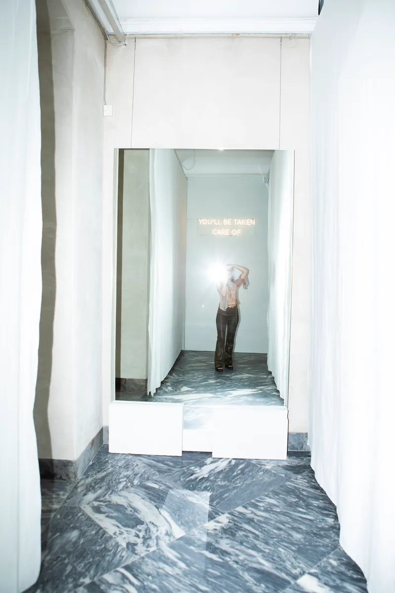 Narrow corridor with white walls and marbled grey flooring leading to a small exhibition alcove