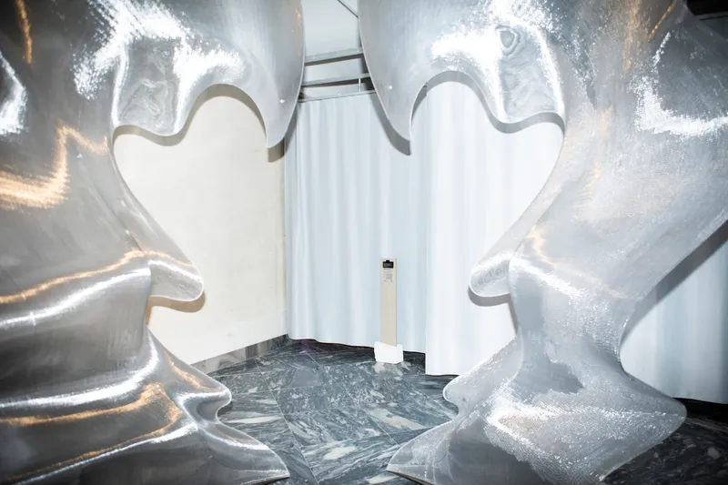 Close-up of inflated metallic sculptural forms arranged in corner space with white curtain backdrop