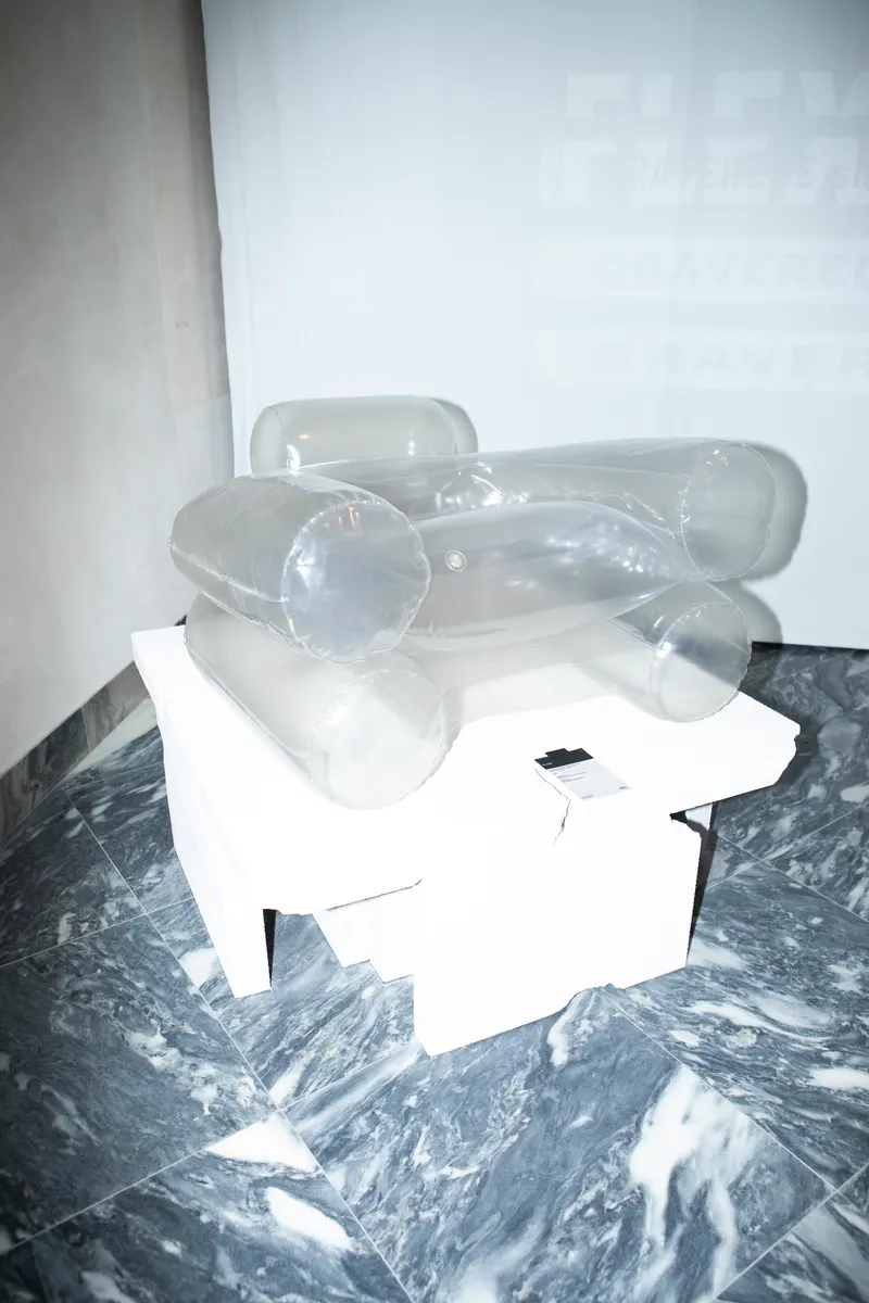 Transparent inflatable sculpture resting on white cubic pedestal over marbled grey floor