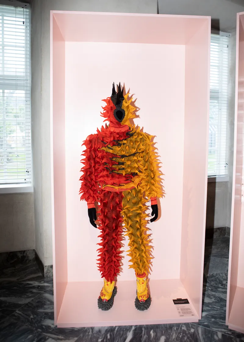 Feathered costume in red and yellow displayed within a pink-lit exhibition alcove