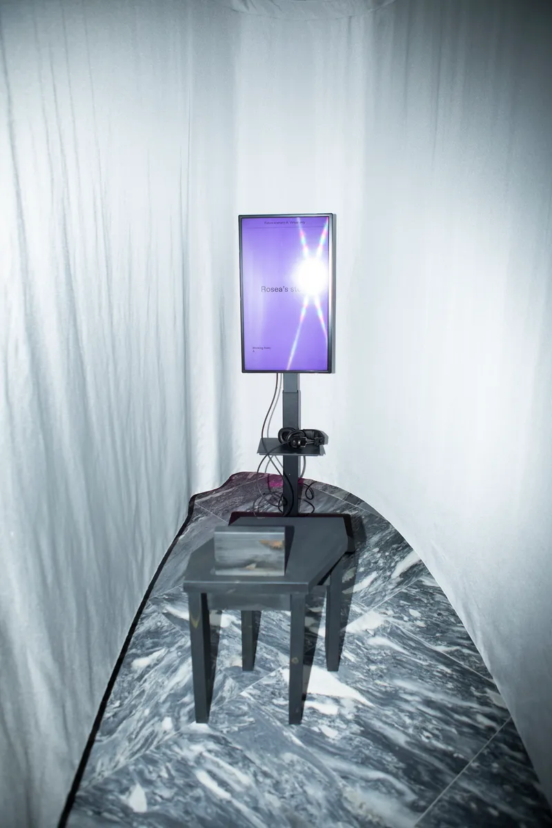 Digital screen on stand and glass table in narrow space lined with translucent curtains