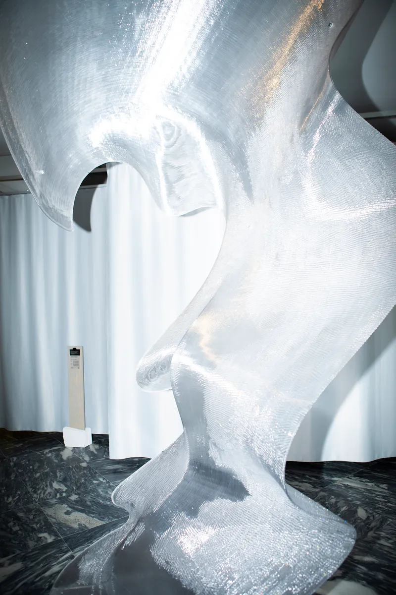 Translucent white sculptural column with spiral ridges rising from black marbled floor