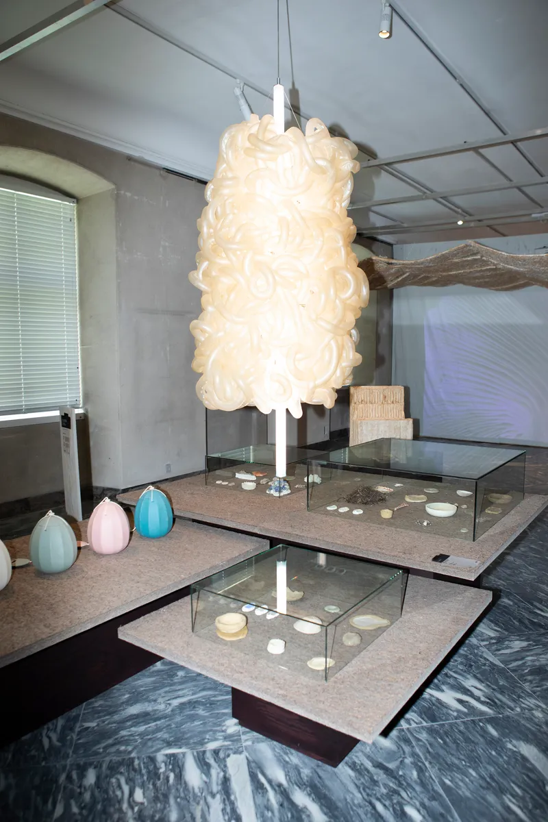 Exhibition space with suspended cream pendant light above terrazzo display tables and glass vitrines