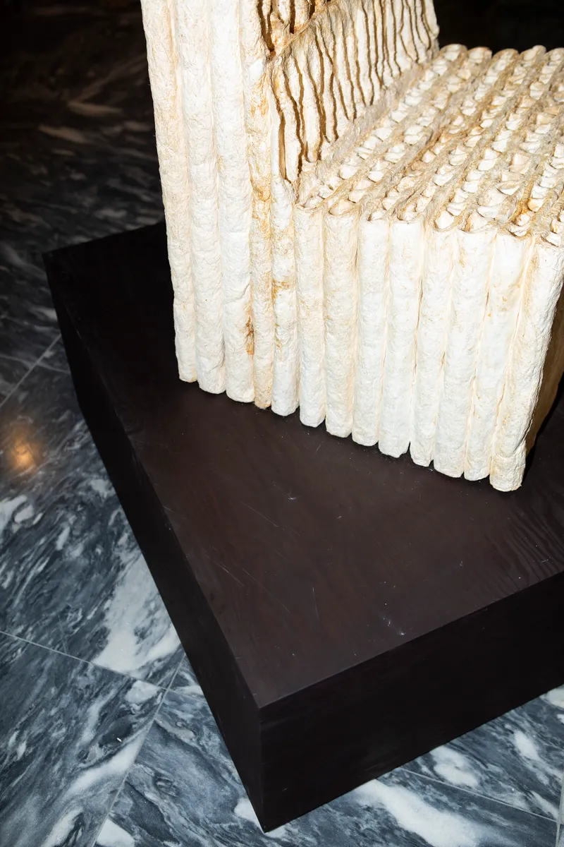 Detail of white cylindrical material sample resting on dark plinth above marbled floor