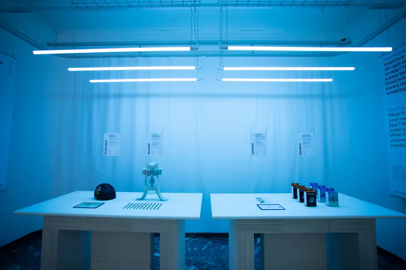 White display table with material samples beneath fluorescent tube lighting and sheer curtain backdrop