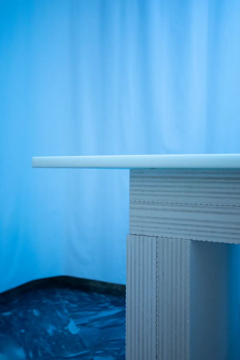 Close-up of corrugated cardboard table edge with white rounded top against a blue curtain