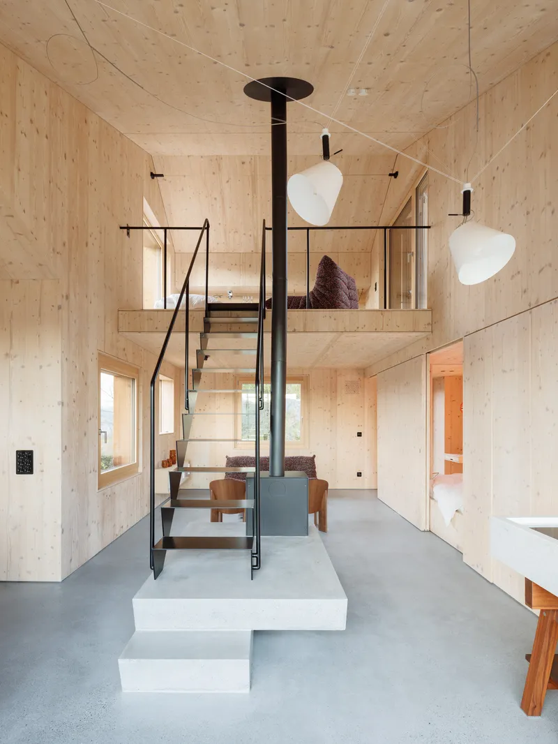 Double-height interior with central black stove pipe and steel staircase leading to sleeping loft above