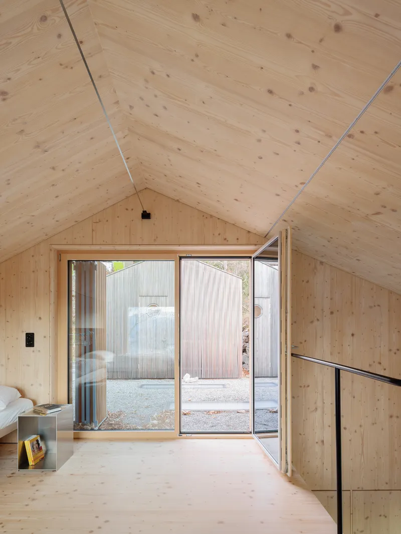 Bedroom loft with sliding glass doors opening to a courtyard with corrugated metal walls in daylight