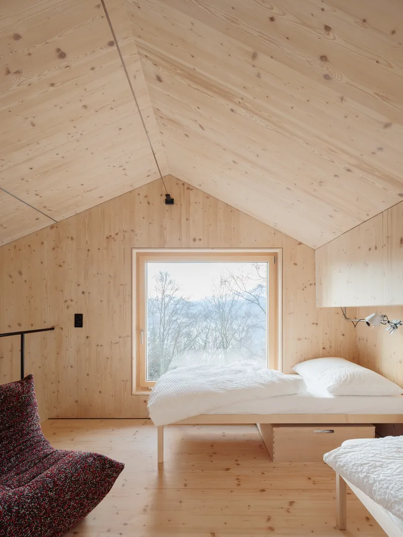 Sleeping alcove with platform bed facing a single window framing bare trees and snowy hills beyond