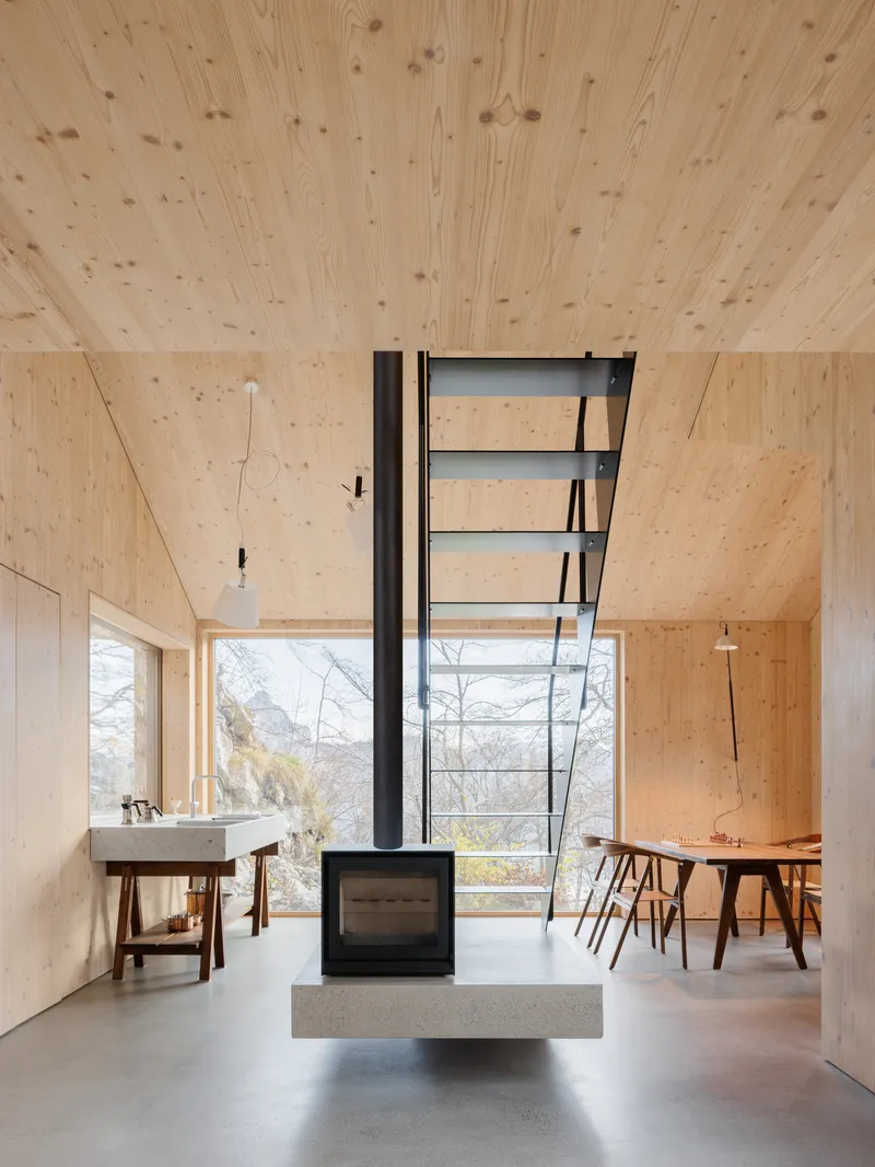 Central freestanding woodstove with black flue pipe beneath a plywood ceiling in the open living space