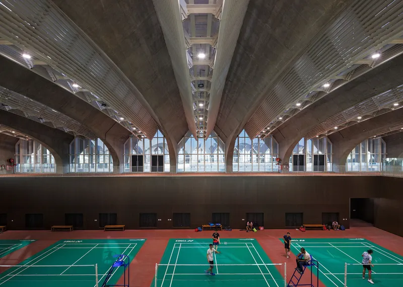 Interior sports hall with badminton courts under ribbed concrete vaults and clerestory windows