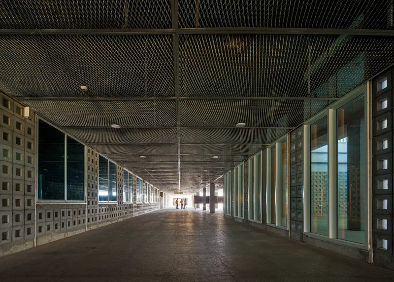 Long corridor with perforated metal ceiling and patterned concrete block walls flanking glazed openings