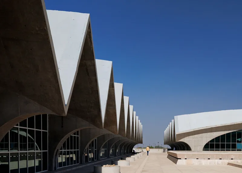 Repeating triangular concrete roof forms creating a rhythmic facade under clear blue sky