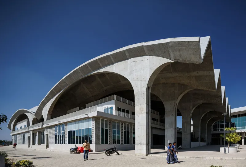 Exterior view of the repeating concrete arches sheltering a glazed ground floor with pedestrians and motorcycles