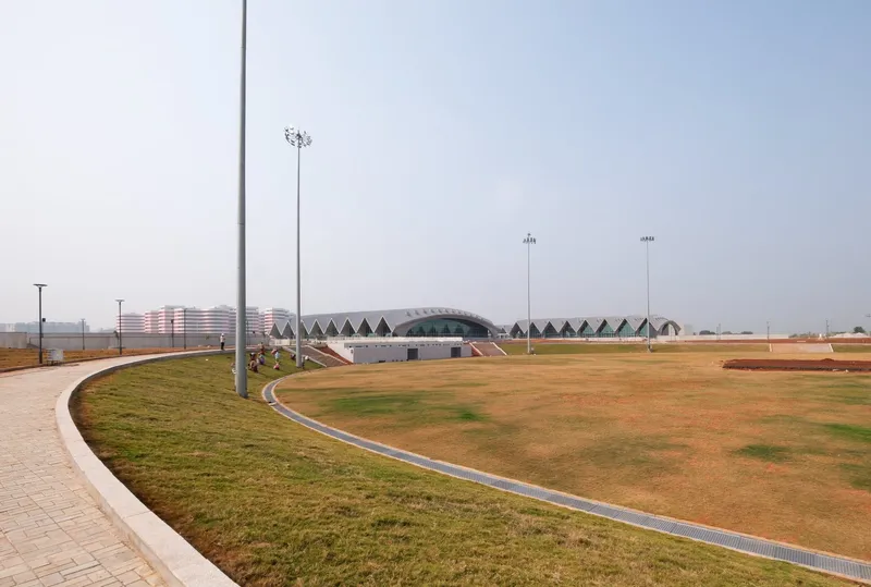 Distant view of the complex with sawtooth roofline across landscaped grounds with patchy grass and lighting towers