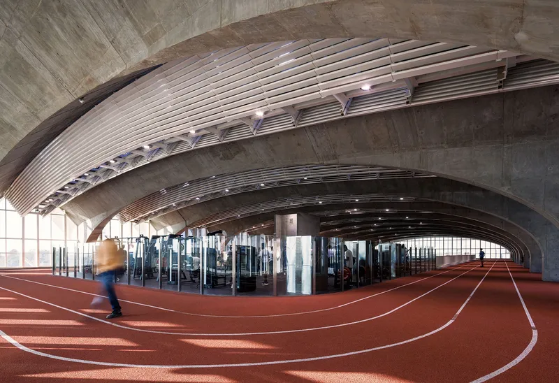 Arched vault ceiling over indoor running track with curved white lane markings and a blurred figure in motion