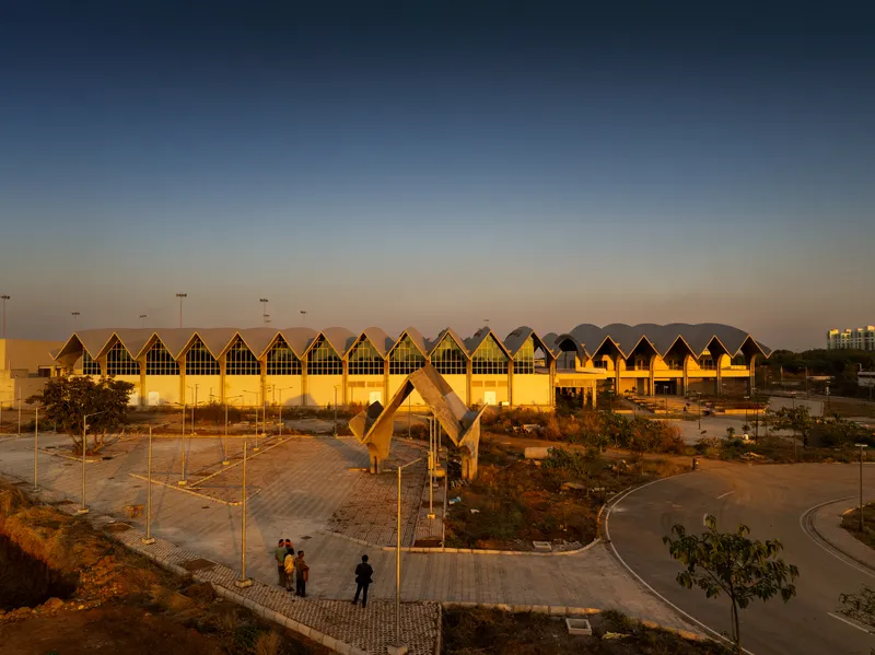 Ground-level view of the zigzag roofline with triangular glazed facades at twilight and visitors approaching