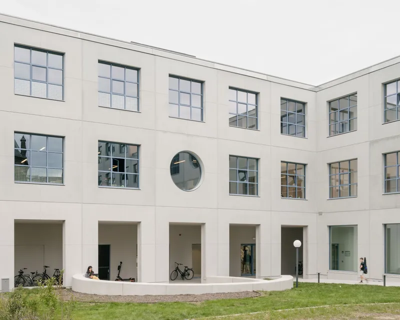 Interior courtyard with white rendered facade, gridded windows, round porthole, and arcade with students and bicycles