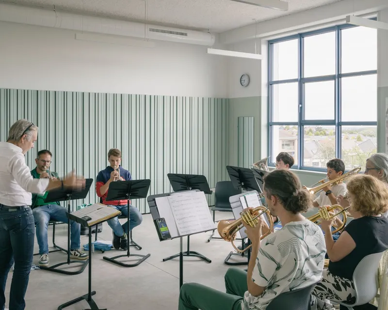 Ensemble rehearsal room with striped green wall panels and musicians seated in a circle