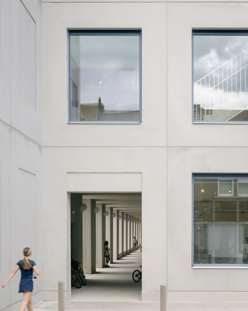 White facade opening framing the colonnade with a woman walking past in afternoon light