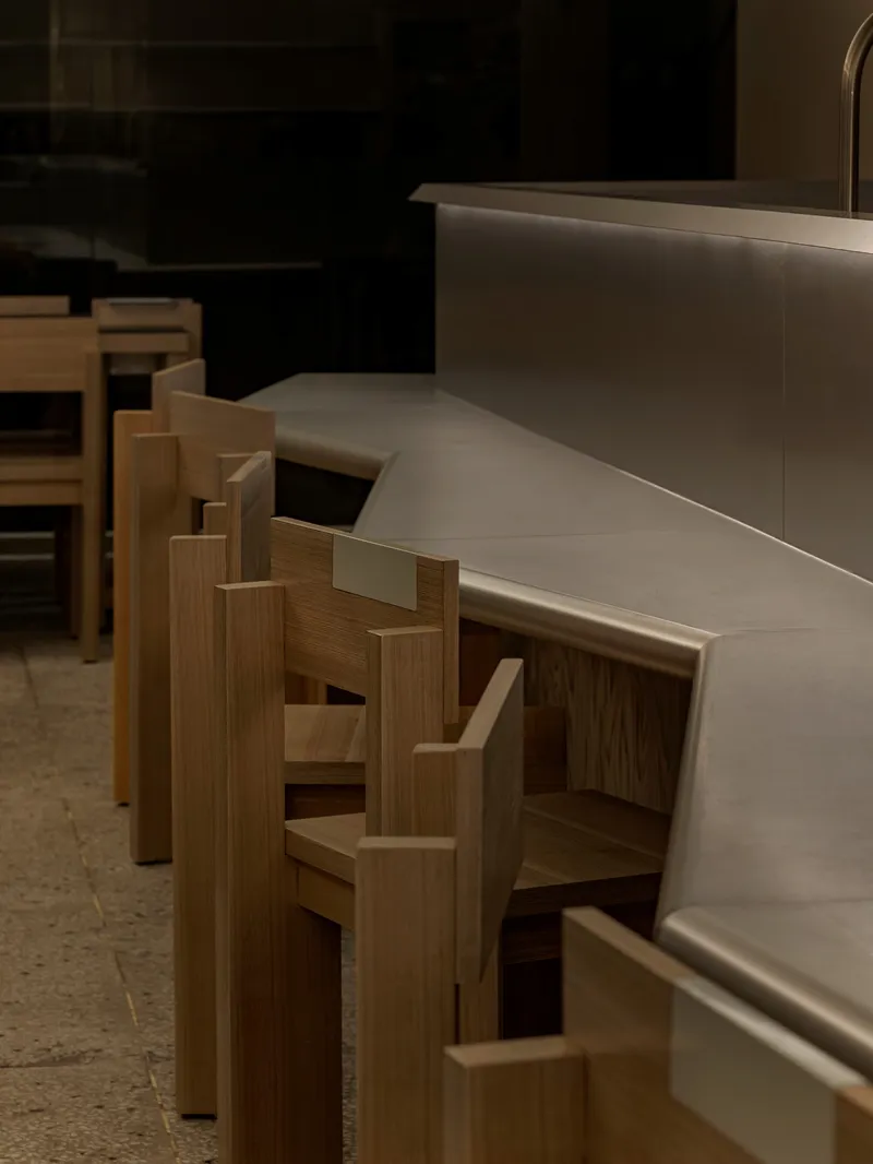 Close-up of timber bar stools with stepped backrests lined along a curved counter edge