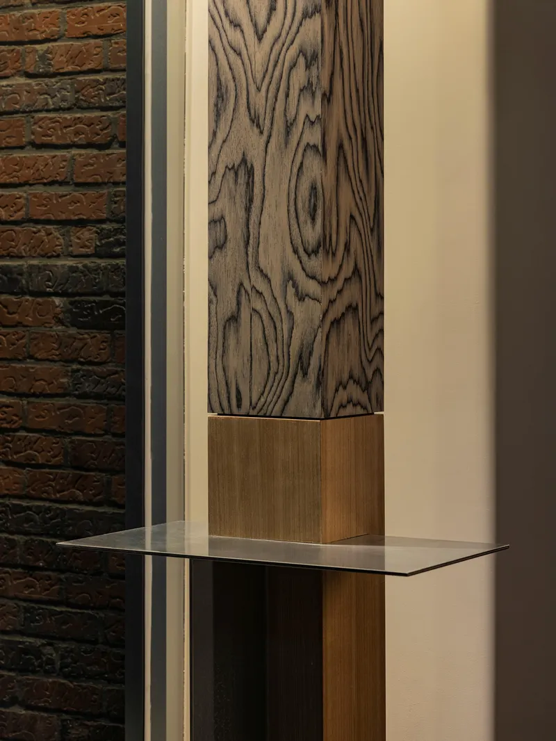 Detail of wood-grained column with glass shelf against exposed brick wall