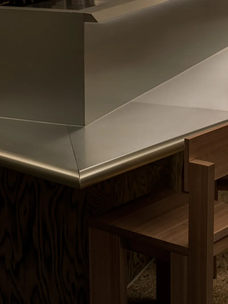 Detail of brushed brass counter edge meeting timber millwork beneath white plaster walls