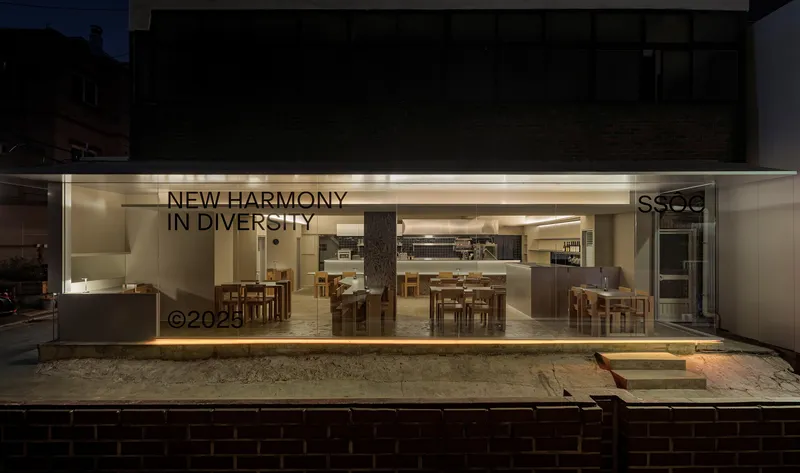 Street view through full-height glass storefront showing dining room interior at dusk
