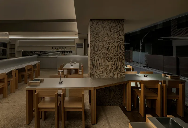 Dining area with timber tables and chairs arranged around a wood-grained column under recessed lighting