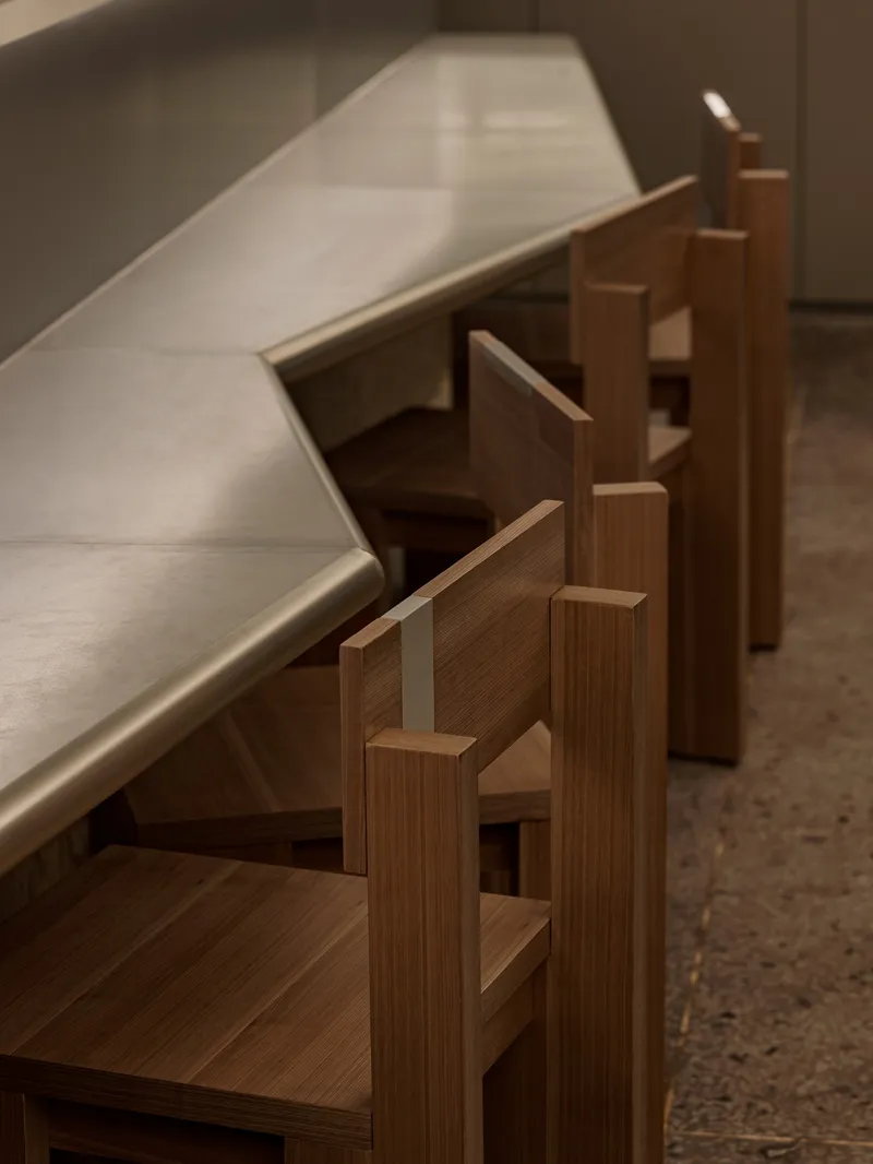 Close-up of stepped timber seating elements along a brushed metal counter in soft light