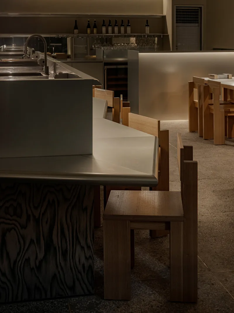 Interior dining area with timber chairs and metal counter beneath warm overhead lighting