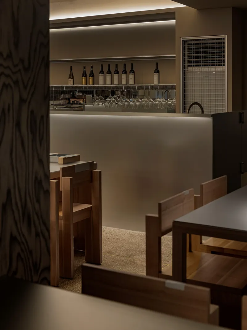 View toward backlit bar counter with wine bottles and terrazzo flooring framed by timber seating