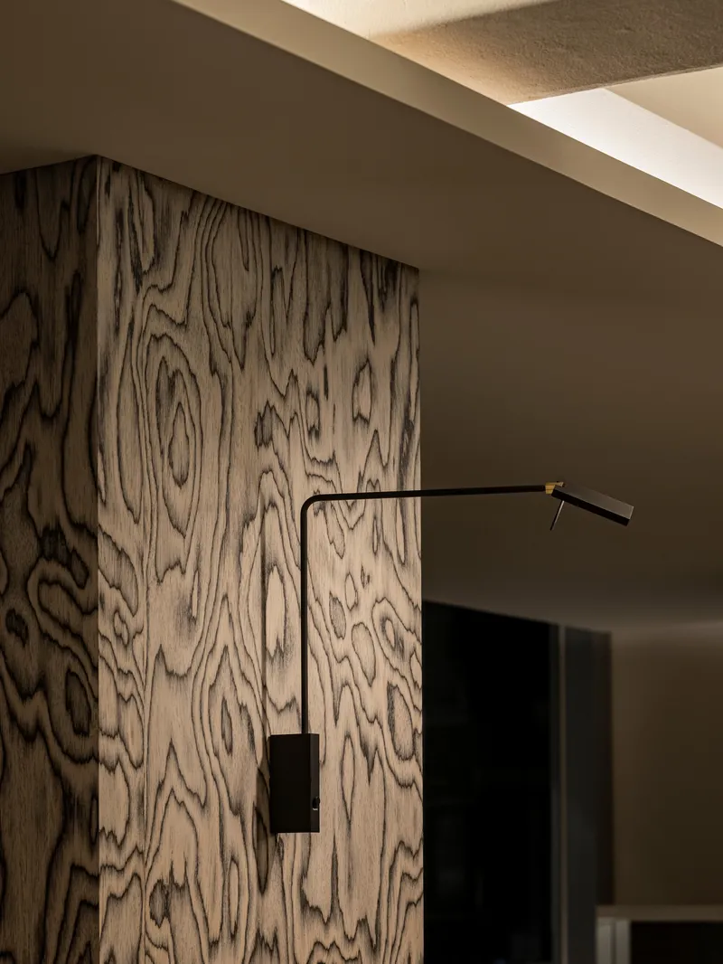 Figured wood grain wall panel with black swing-arm wall sconce in recessed ceiling