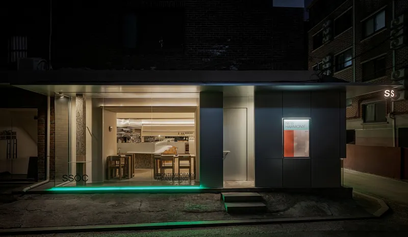 Street facade at night showing glazed storefront with green ground lighting and black metal cladding