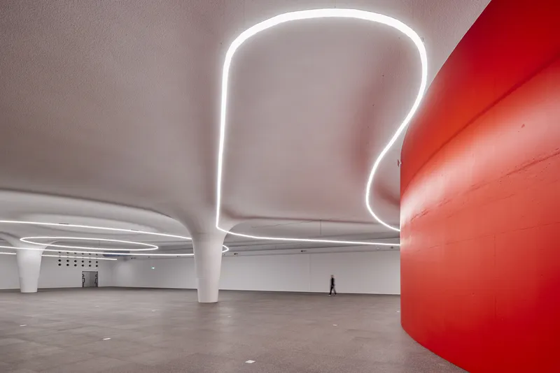 Interior gallery space with white curved columns and organic LED light fixtures with a figure walking