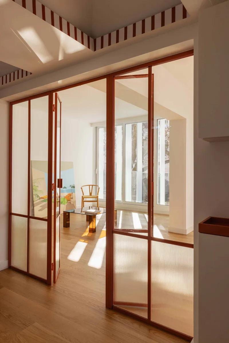 Timber-framed glass doors opening to a sunlit room with wishbone chair visible beyond