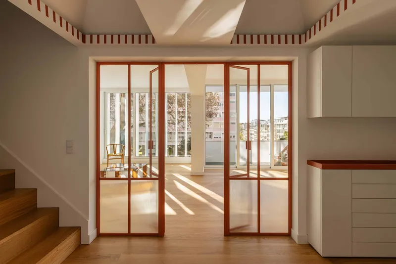 Red-framed folding glass doors opening to a terrace with striped ceiling trim and natural light