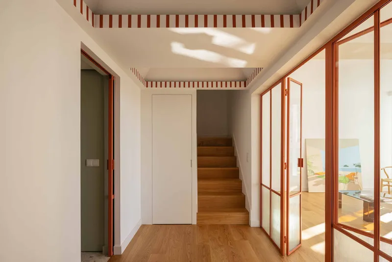 View from hallway through open red-framed doors to a sunlit room with ocean painting