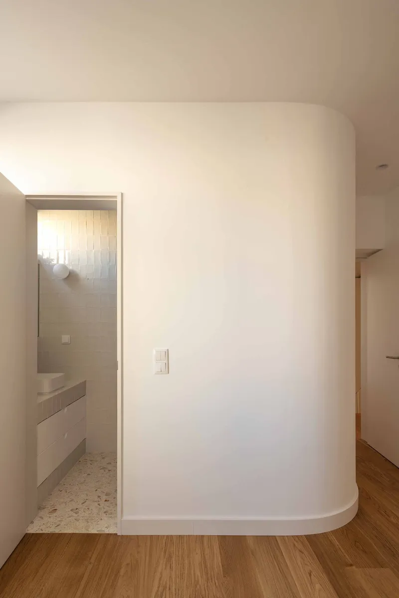 Curved white partition wall with doorway opening to tiled bathroom beyond