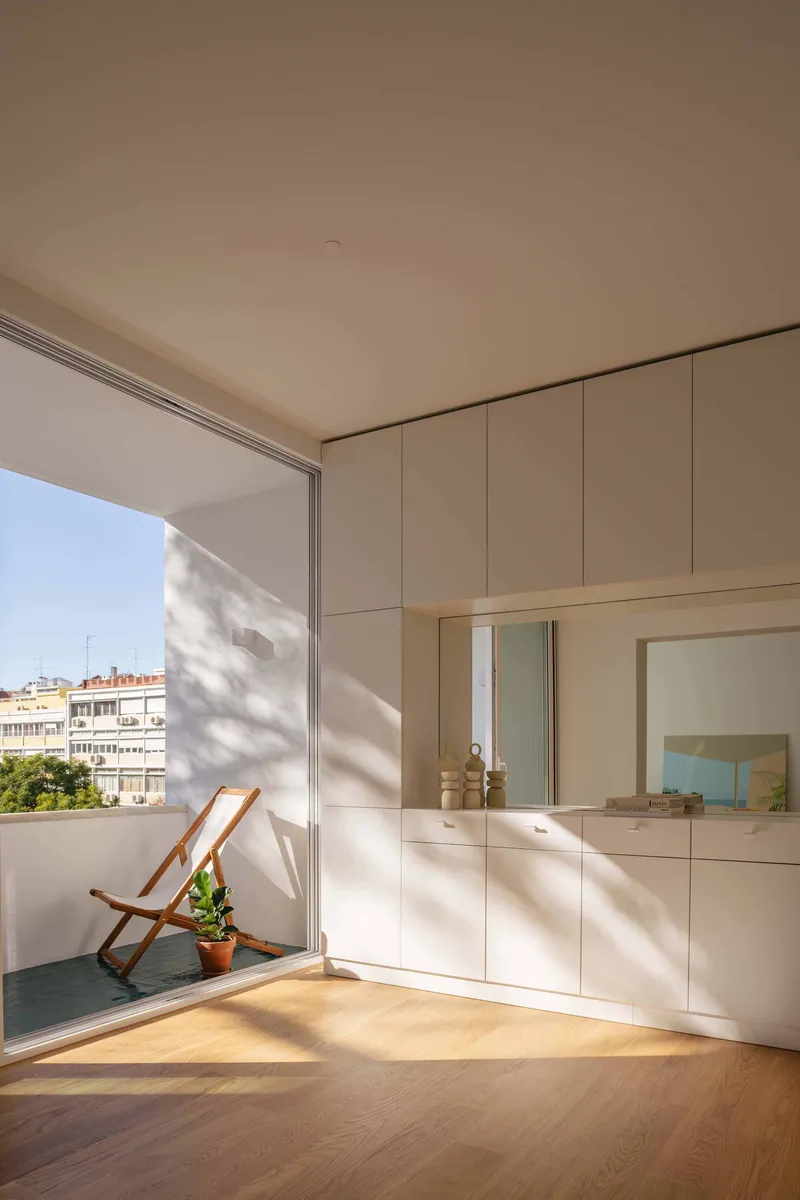 Interior room opening to terrace with folding chair and built-in cabinetry in afternoon sun