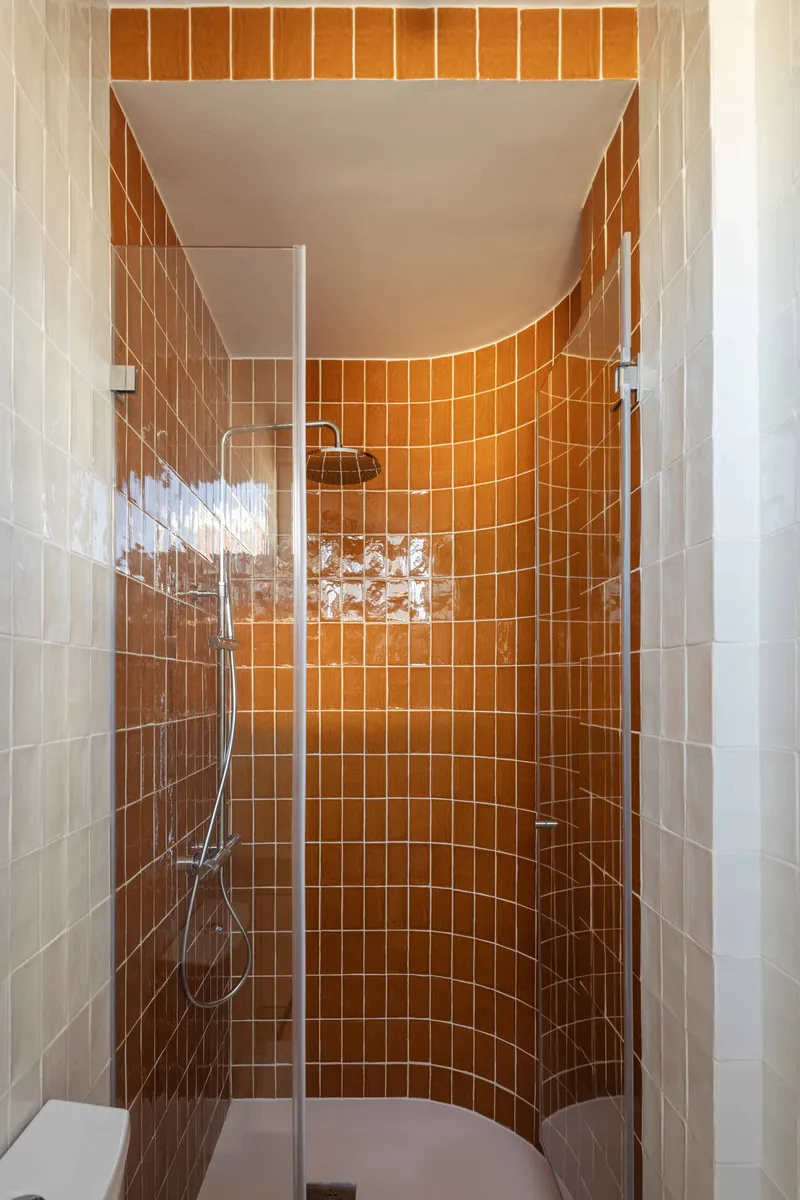 Curved shower stall lined with orange square tiles and fitted with chrome fixtures