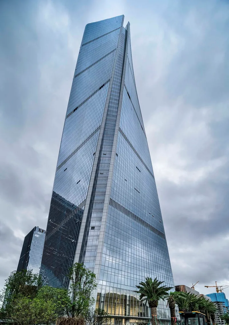 Full height view of the tapered glass tower with diagonal bracing lines under overcast sky