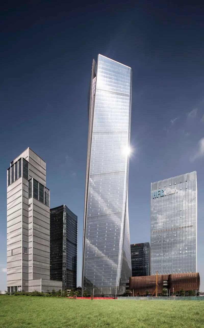 Twisted glass tower rising above surrounding buildings and a foreground lawn on a clear day