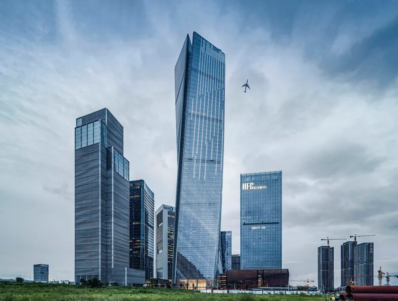 Cluster of glass towers with twisted geometries under a cloudy sky with a plane passing overhead