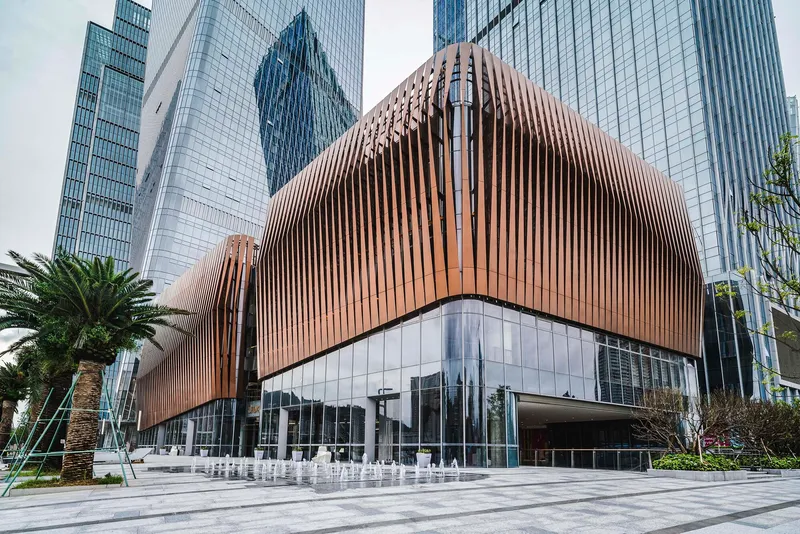 Curved copper-clad podium with vertical fins above a glazed base and plaza fountain with palm trees
