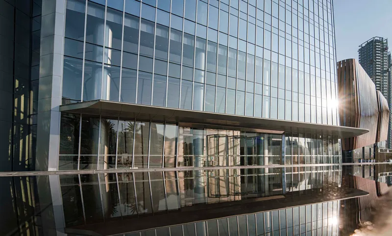 Reflecting pool mirroring the glass curtain wall and elevated pedestrian bridge at the tower base