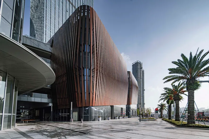 Side view of the rippling metal-clad volume beside a covered walkway and rows of palm trees